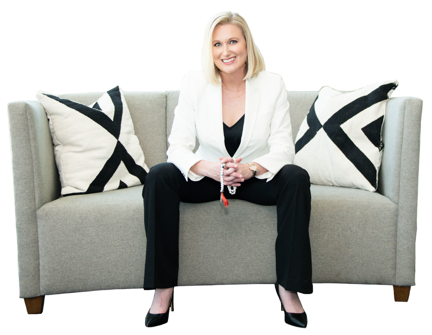 Katherine M. Sauer wearing a white blazer and holding a yoga mala, sitting on a couch